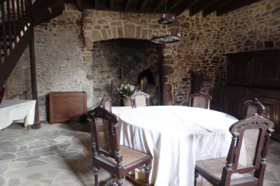 Cave voûtée en pierre avec tonneaux en bois, tabourets rustiques et escalier menant à l'extérieur.