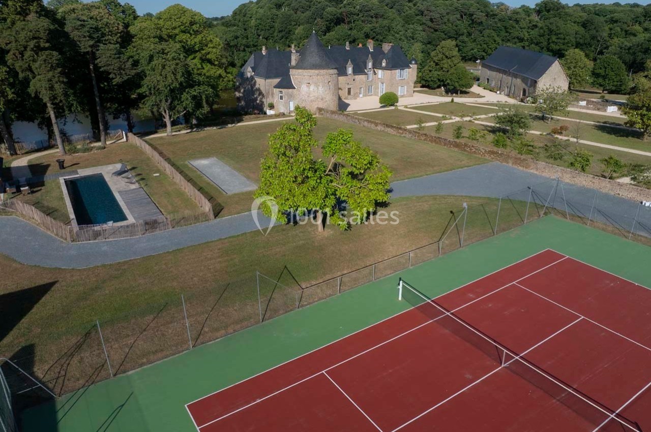 Vue aérienne d'un domaine avec un court de tennis, une piscine, des bâtiments en pierre et un parc arboré.