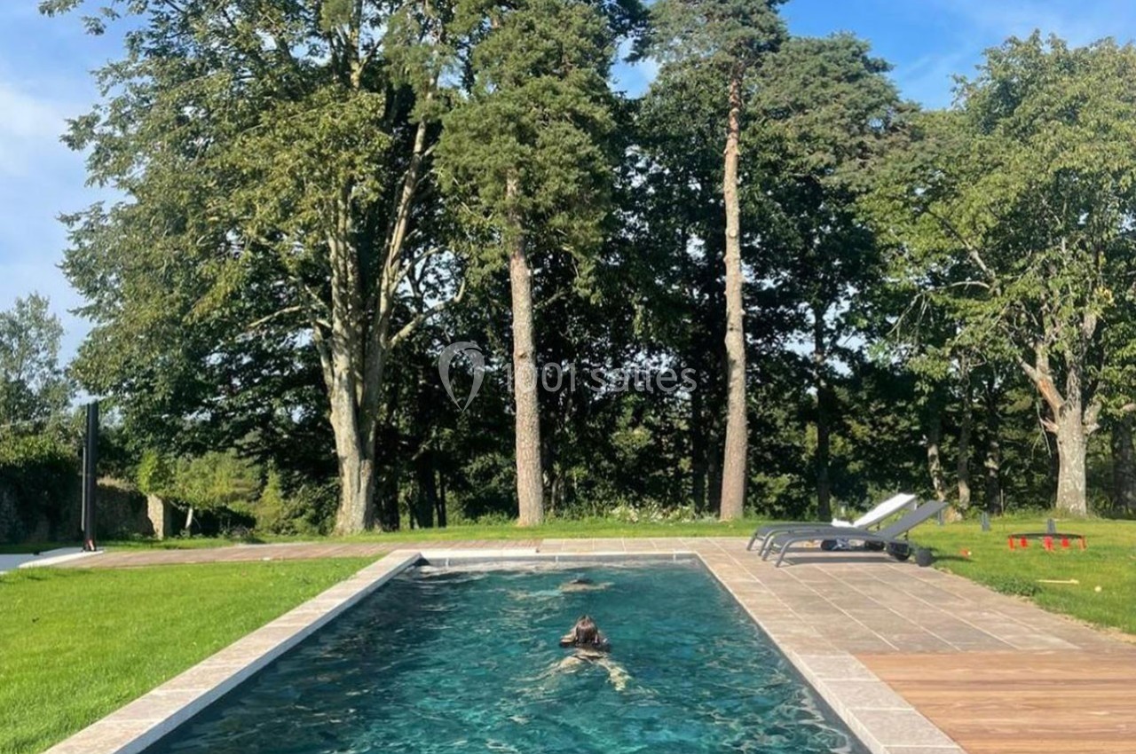 Une personne nage dans une piscine extérieure entourée de pelouse, avec des arbres en arrière-plan.