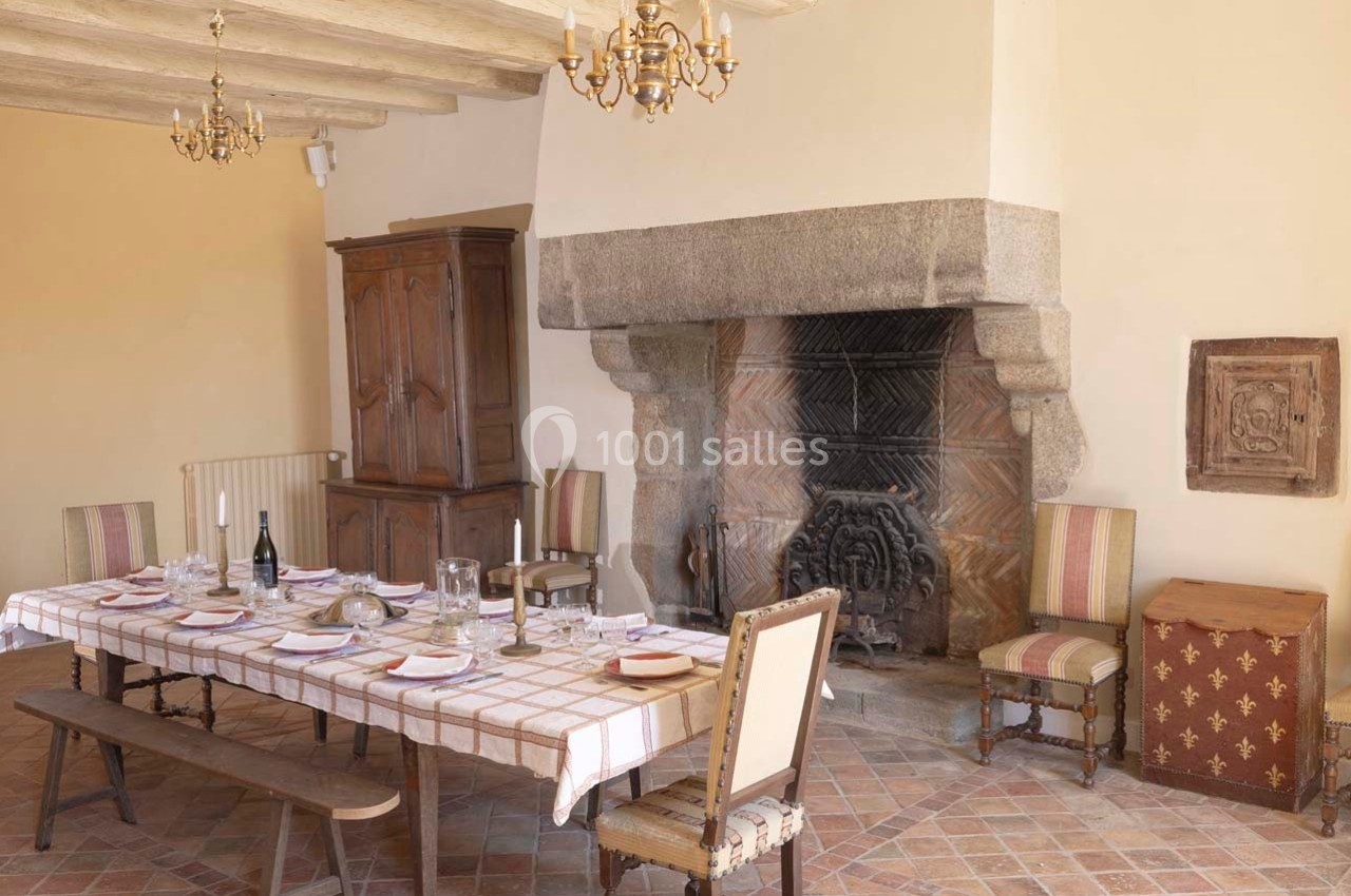 Salle à manger rustique avec grande cheminée en pierre, table dressée et mobilier en bois et tissu rayé.