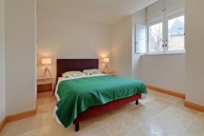 Cave voûtée en pierre avec tonneaux en bois, tabourets rustiques et escalier menant à l'extérieur.