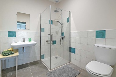 Cave voûtée en pierre avec tonneaux en bois, tabourets rustiques et escalier menant à l'extérieur.