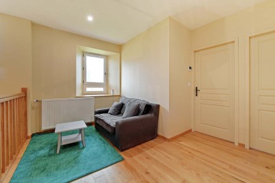 Cave voûtée en pierre avec tonneaux en bois, tabourets rustiques et escalier menant à l'extérieur.