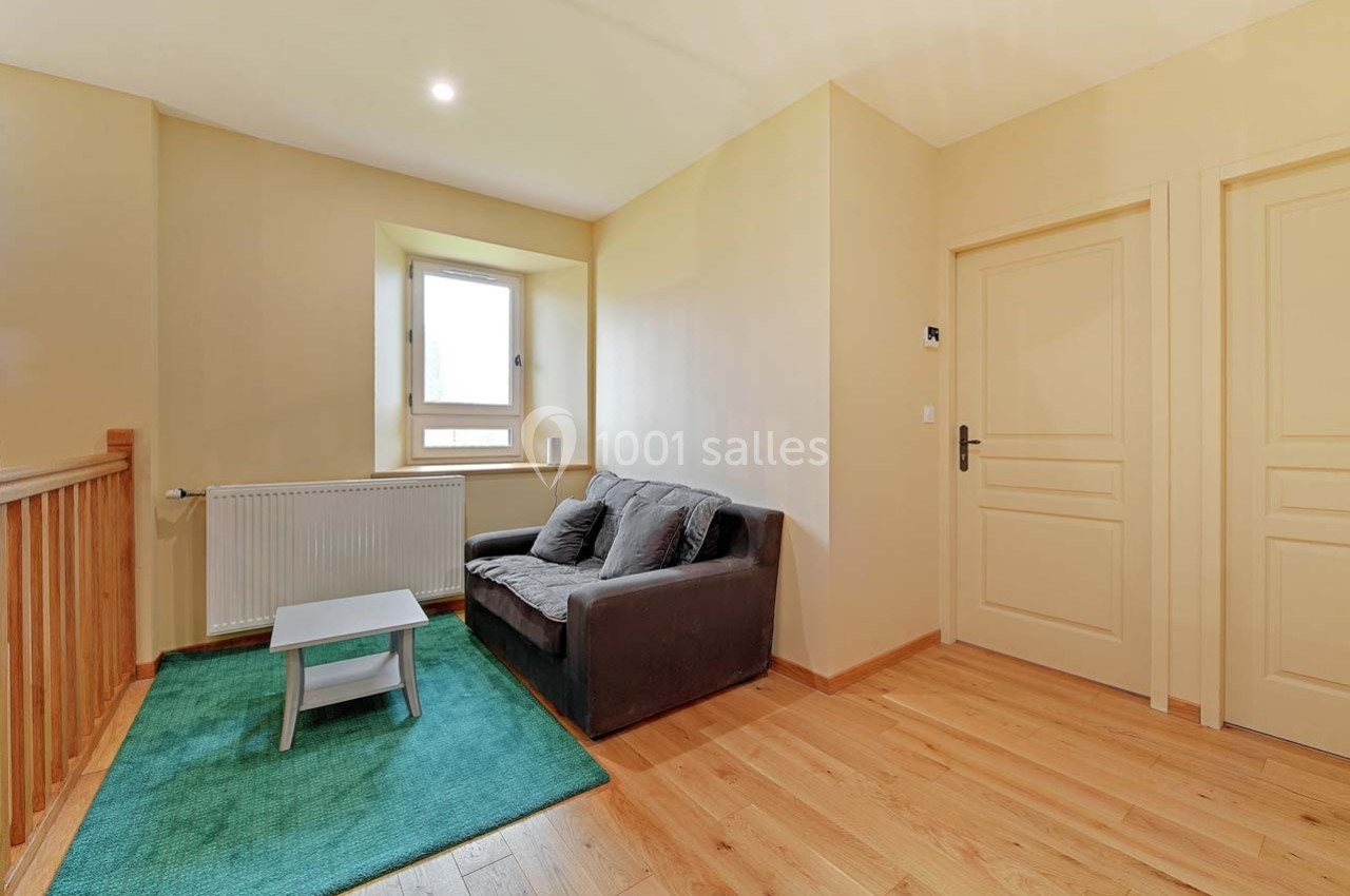 Petit salon avec canapé gris, table basse sur un tapis vert, parquet en bois clair et mur beige avec deux portes.