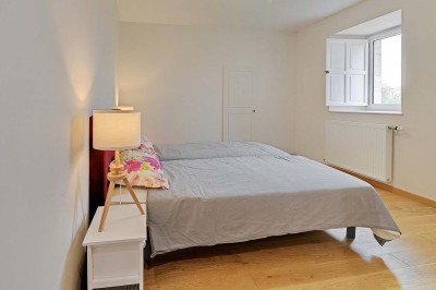 Cave voûtée en pierre avec tonneaux en bois, tabourets rustiques et escalier menant à l'extérieur.