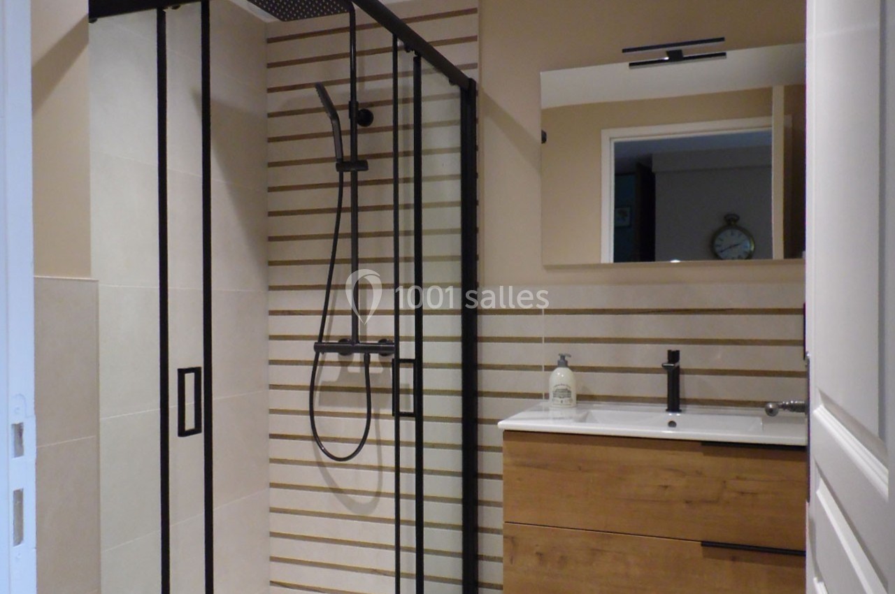 Salle de bain moderne avec douche à paroi vitrée noire, meuble en bois et miroir au-dessus du lavabo.