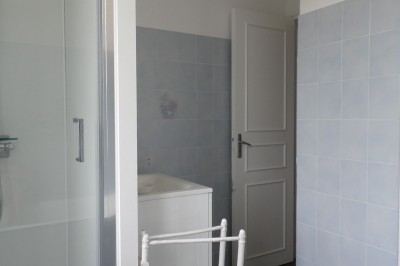 Cave voûtée en pierre avec tonneaux en bois, tabourets rustiques et escalier menant à l'extérieur.