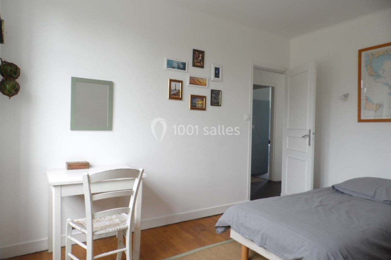Chambre lumineuse avec un lit simple, un bureau blanc, des cadres accrochés au mur et une carte encadrée.