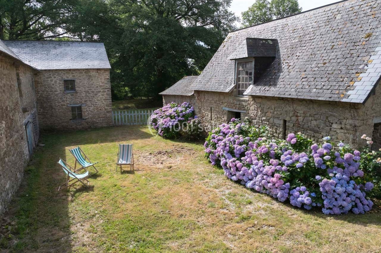 Cour enherbée entourée de bâtiments en pierre, avec des hortensias en fleurs et deux chaises longues colorées.