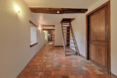 Cave voûtée en pierre avec tonneaux en bois, tabourets rustiques et escalier menant à l'extérieur.