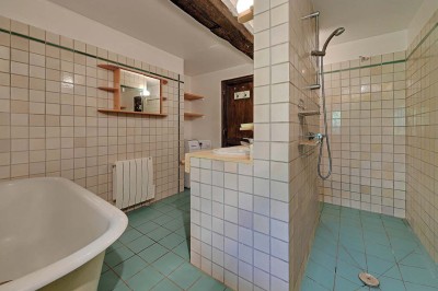 Cave voûtée en pierre avec tonneaux en bois, tabourets rustiques et escalier menant à l'extérieur.