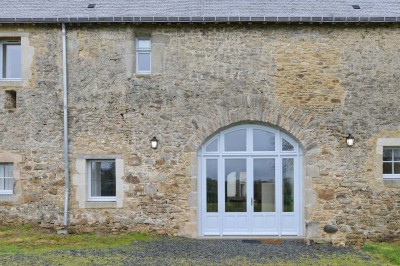 Cave voûtée en pierre avec tonneaux en bois, tabourets rustiques et escalier menant à l'extérieur.