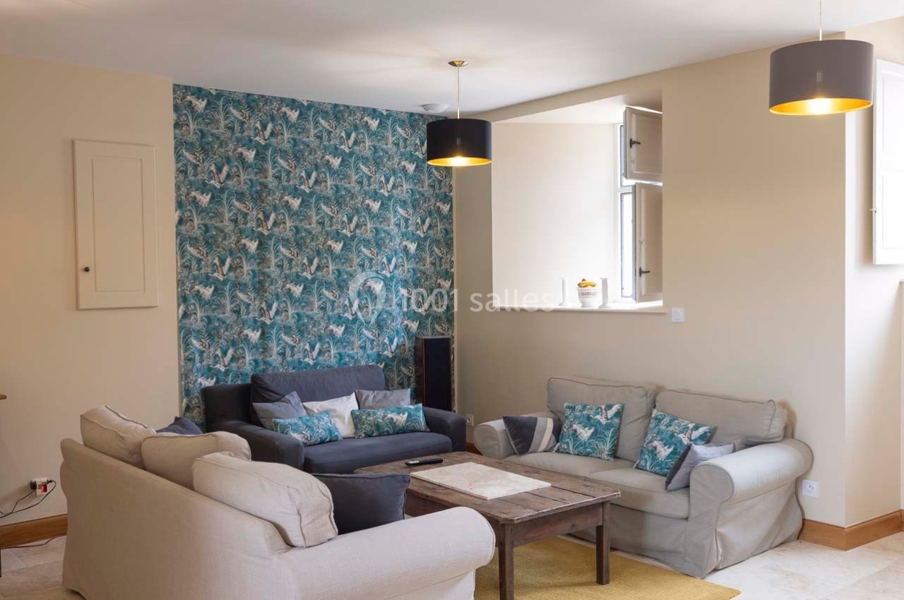 Salon lumineux avec canapé beige et gris, table basse en bois, mur décoré de papier peint à motifs tropicaux.