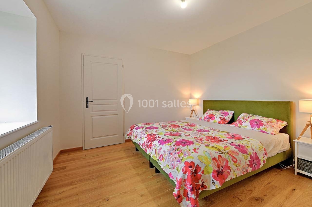 Chambre lumineuse avec lit double, linge de lit à motifs floraux, parquet en bois clair et deux lampes de chevet.