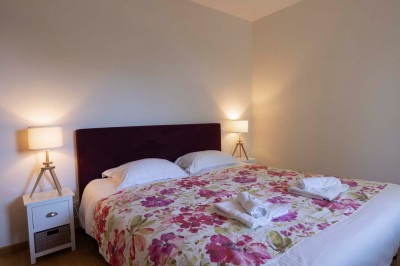 Cave voûtée en pierre avec tonneaux en bois, tabourets rustiques et escalier menant à l'extérieur.