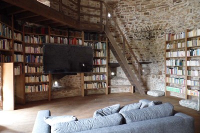 Cave voûtée en pierre avec tonneaux en bois, tabourets rustiques et escalier menant à l'extérieur.