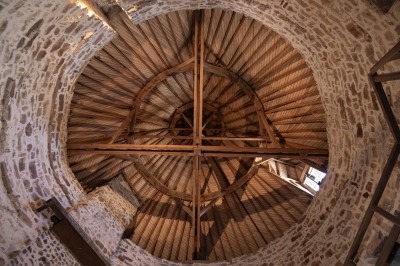 Cave voûtée en pierre avec tonneaux en bois, tabourets rustiques et escalier menant à l'extérieur.
