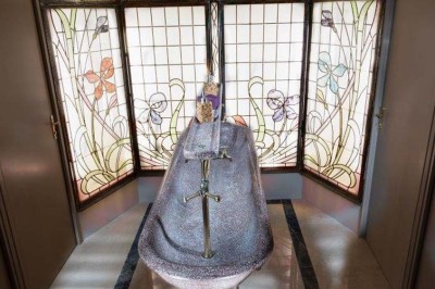 Statue moderne près d'un escalier en marbre et d'un ascenseur à portes vitrées dans un hall lumineux.