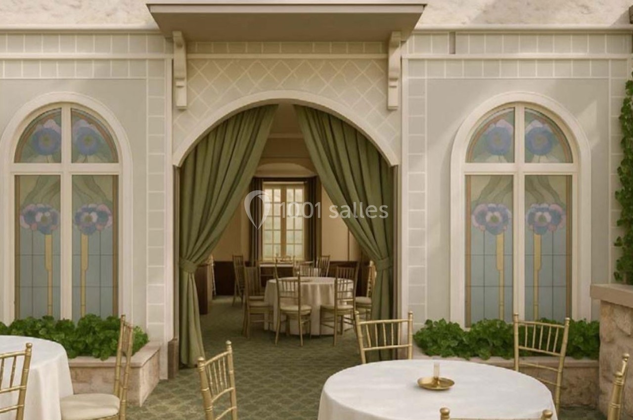 Salle élégante avec tables rondes dressées, chaises dorées, vitraux fleuris et rideaux verts encadrant une entrée voûtée.
