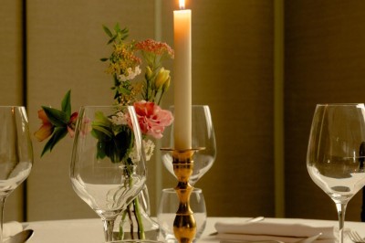 Bougie allumée sur un chandelier doré au centre d'une table dressée avec verres, fleurs et serviettes.