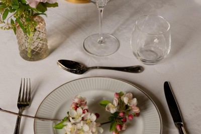 Bougie allumée sur un chandelier doré au centre d'une table dressée avec verres, fleurs et serviettes.