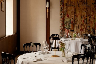 Salle de restaurant élégante avec tables dressées, chaises noires et décoration murale en treillis beige.