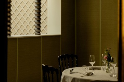 Salle de restaurant élégante avec tables dressées, chaises noires et décoration murale en treillis beige.
