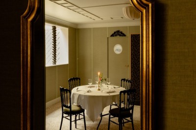 Salle de restaurant élégante avec tables dressées, chaises noires et décoration murale en treillis beige.