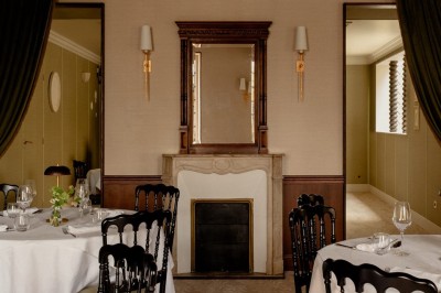 Salle de restaurant élégante avec tables dressées, chaises noires et décoration murale en treillis beige.
