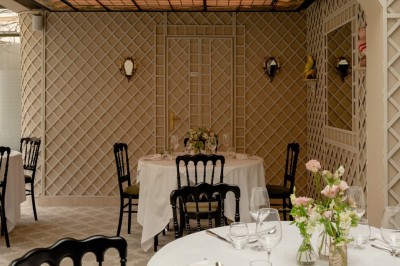 Salle de restaurant élégante avec tables dressées, chaises noires et décoration murale en treillis beige.