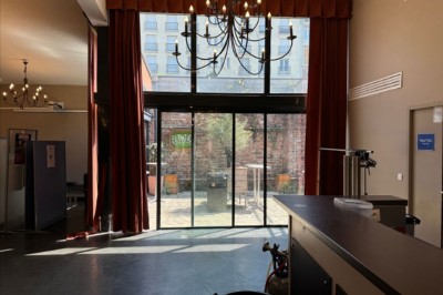 Salle de réception avec tables rondes dressées, nappes colorées et éclairage chaleureux par des lustres suspendus.