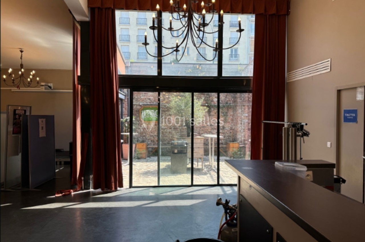 Intérieur lumineux avec de grandes baies vitrées donnant sur une cour extérieure, décoré de rideaux rouges et lustres.