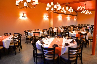 Salle de réception avec tables rondes dressées, nappes colorées et éclairage chaleureux par des lustres suspendus.