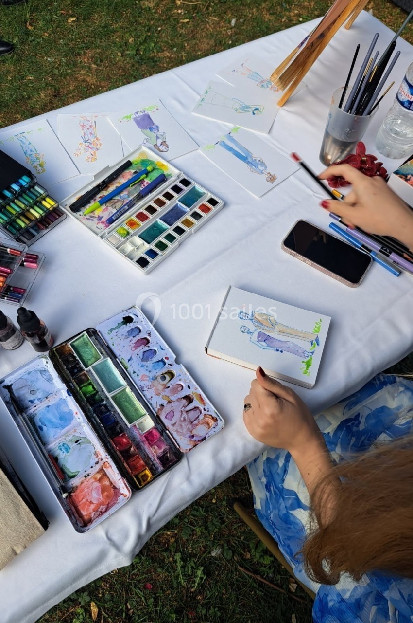 Une personne peint une illustration à l'aquarelle sur une table avec des fournitures artistiques et des croquis.