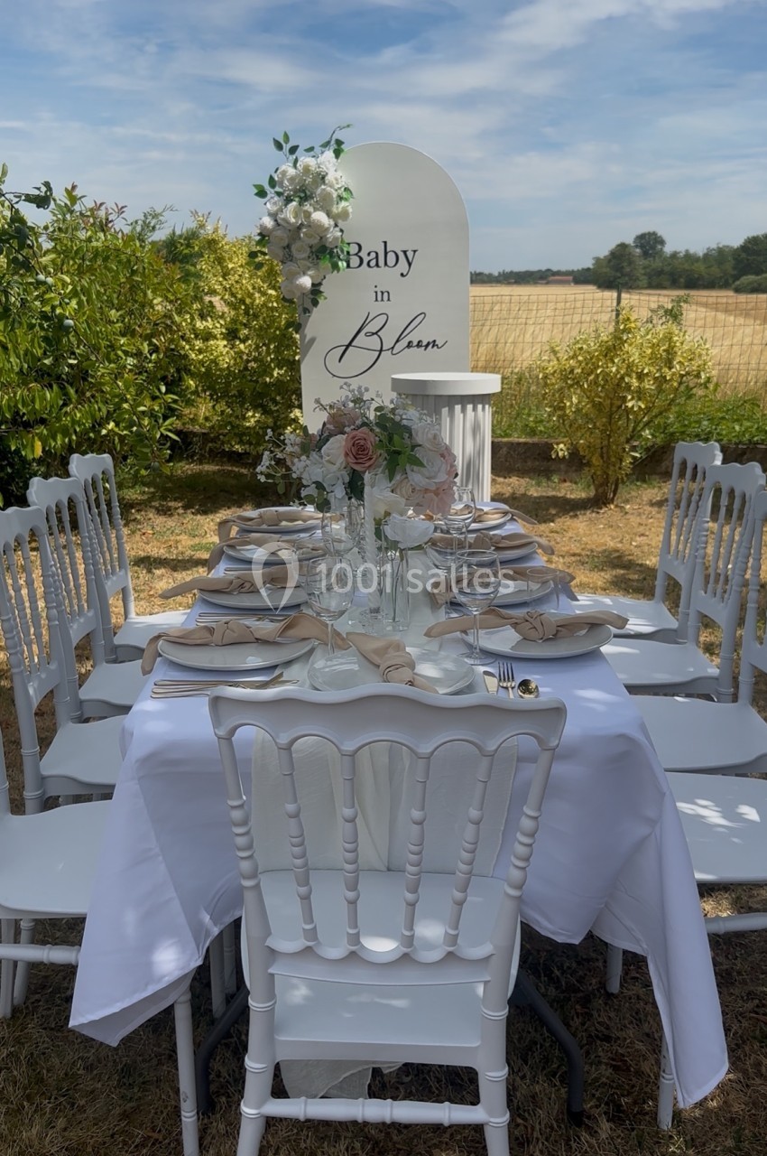 Table décorée pour une fête en plein air, avec nappes blanches, fleurs et panneau ’Baby in Bloom’ en arrière-plan.