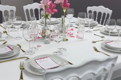 Table élégamment dressée avec nappes blanches, vaisselle raffinée, bougies roses et décoration florale assortie.