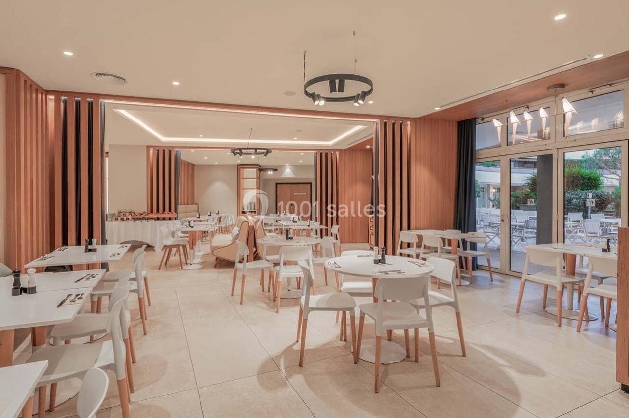 Salle de restaurant lumineuse avec des tables et chaises blanches, décor moderne en bois clair, vue sur une terrasse…