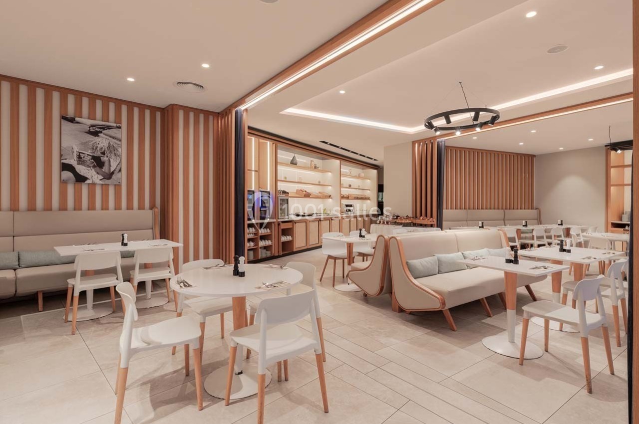 Salle de restaurant moderne avec tables blanches, chaises assorties et éclairage chaleureux, décorée de panneaux en bois…