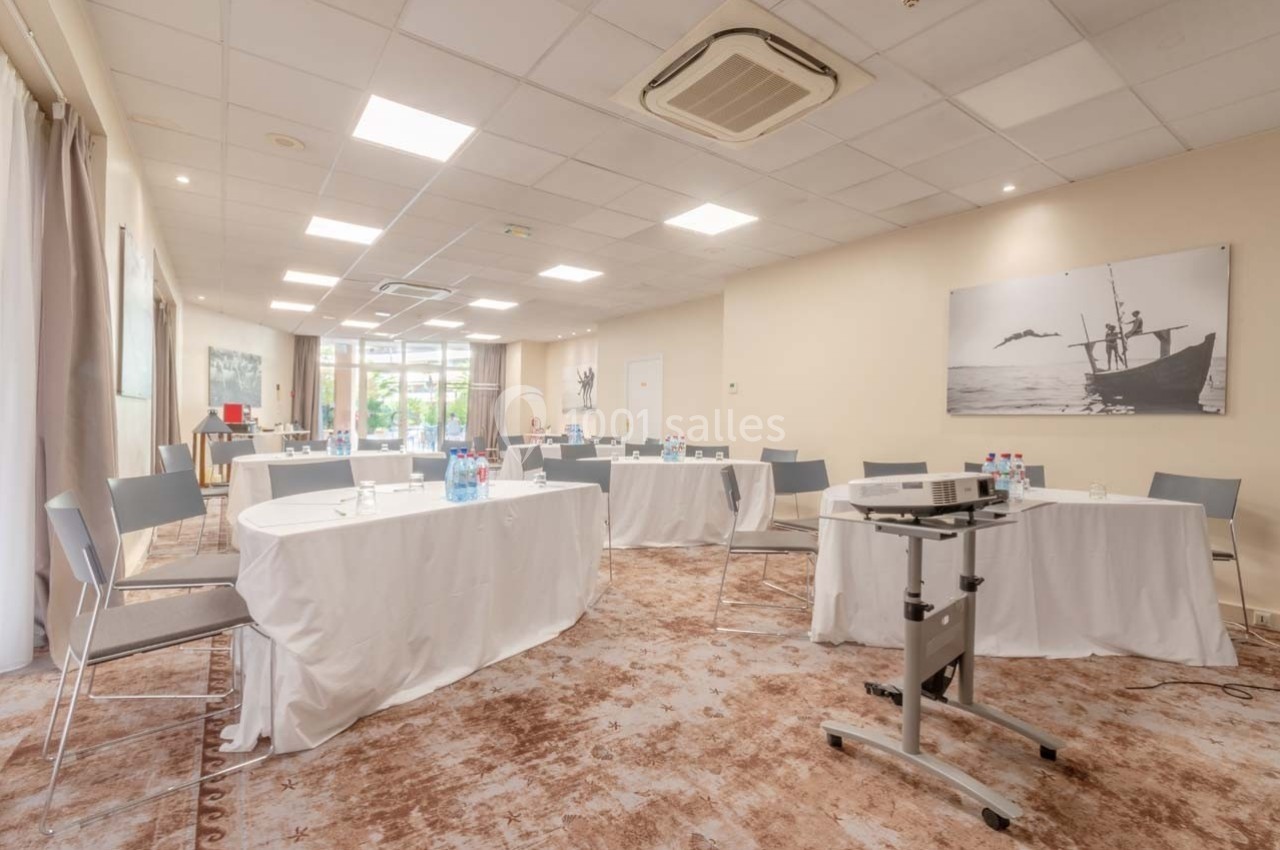 Salle de réunion lumineuse avec tables ovales recouvertes de nappes blanches, chaises et matériel de présentation.