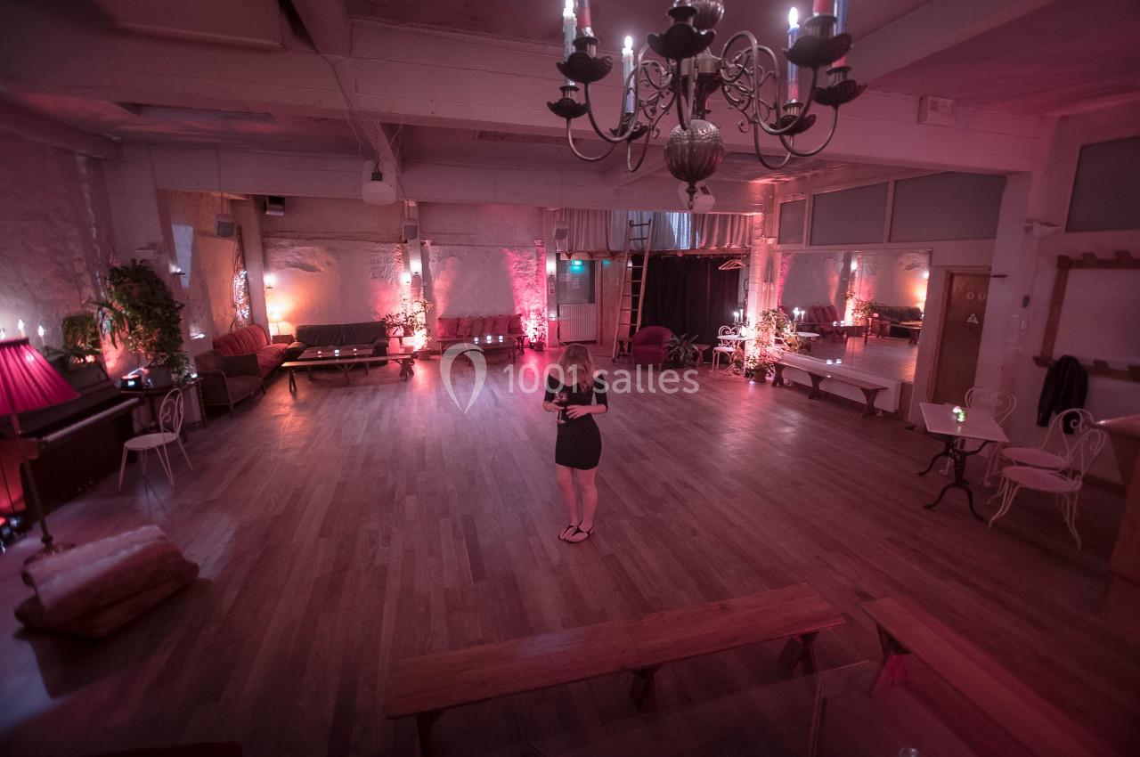Une femme seule lit un livre au centre d'une grande salle éclairée par des lumières tamisées et un lustre.
