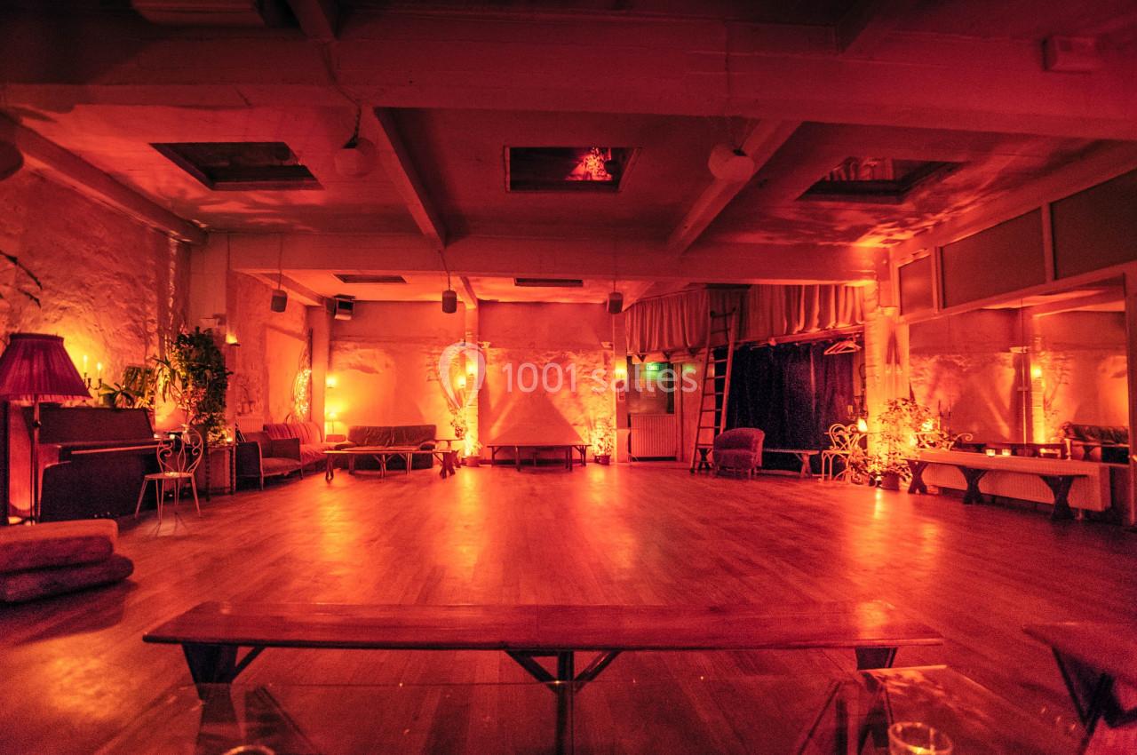 Salle spacieuse avec éclairage tamisé orange, murs en pierre, bancs en bois et décorations végétales.