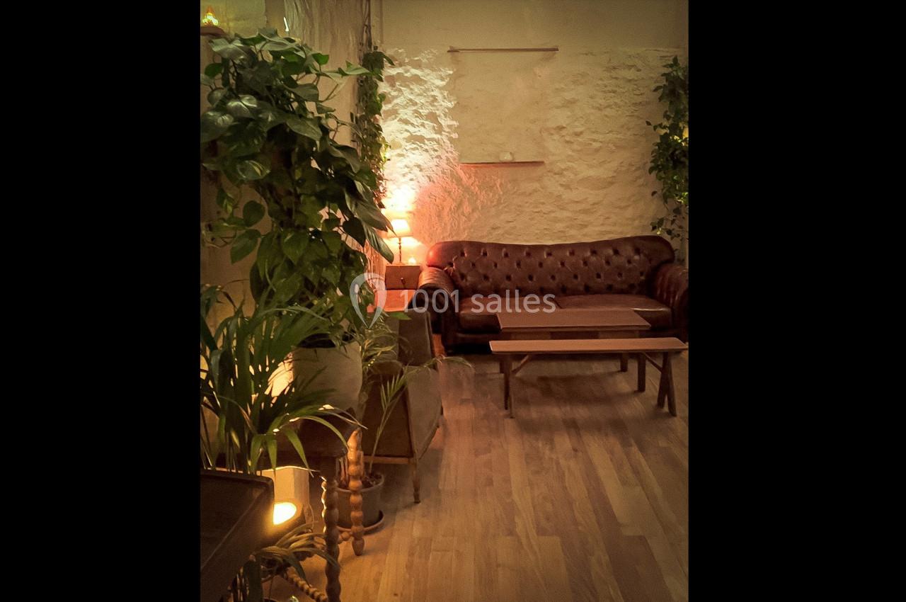 Canapé en cuir marron dans un salon cosy avec plantes vertes, murs en pierre et éclairage tamisé.
