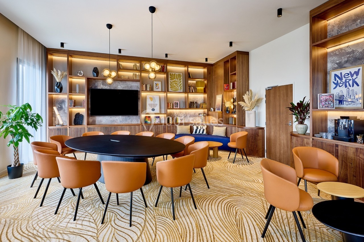 Salle de réunion moderne avec table ronde, chaises en cuir orange, étagères décorées et éclairage suspendu.