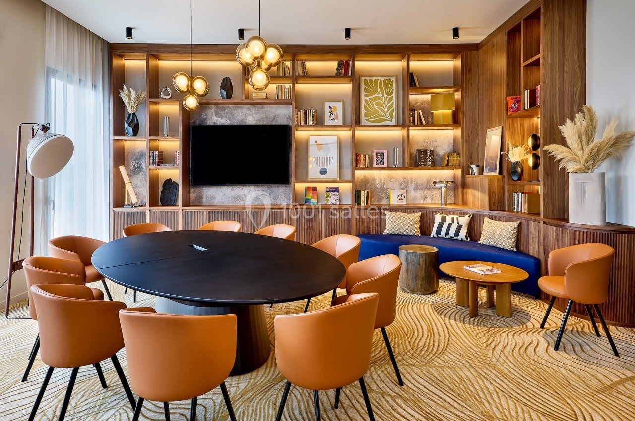 Salle de réunion moderne avec table ronde, chaises orange, étagères en bois éclairées et décoration contemporaine.
