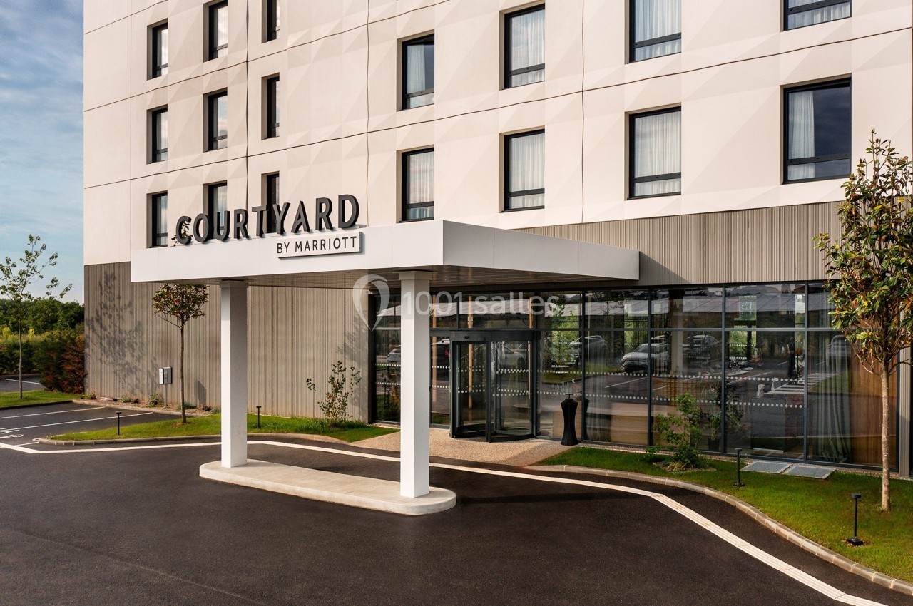 Façade d'un hôtel moderne avec enseigne ’Courtyard by Marriott’, entrée vitrée et aménagement paysager.