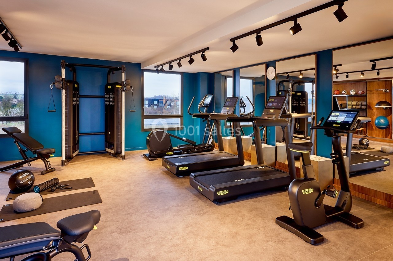 Salle de sport moderne avec tapis de course, machines de musculation et équipements variés, éclairée par des spots.