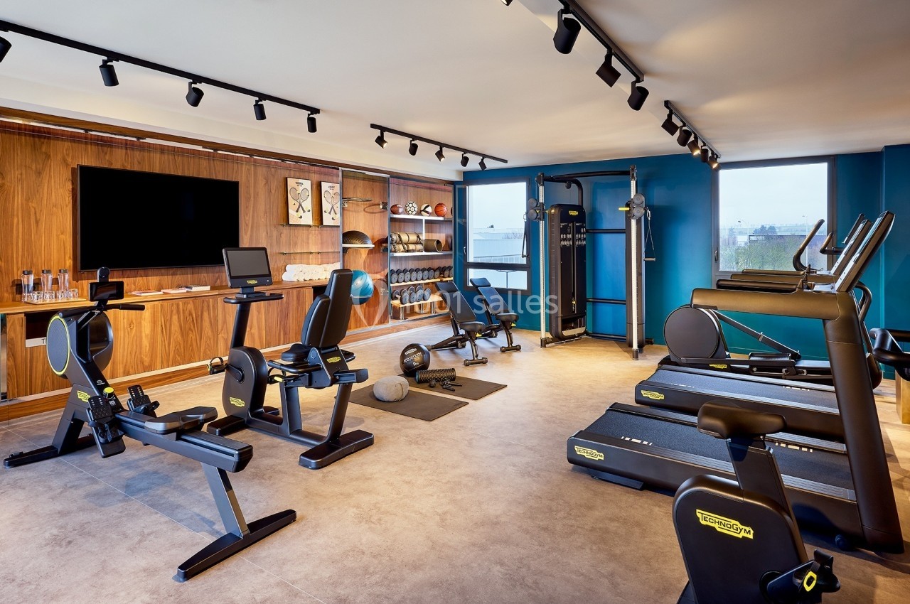 Salle de sport moderne équipée de tapis de course, vélos, rameurs, haltères et machines de musculation.