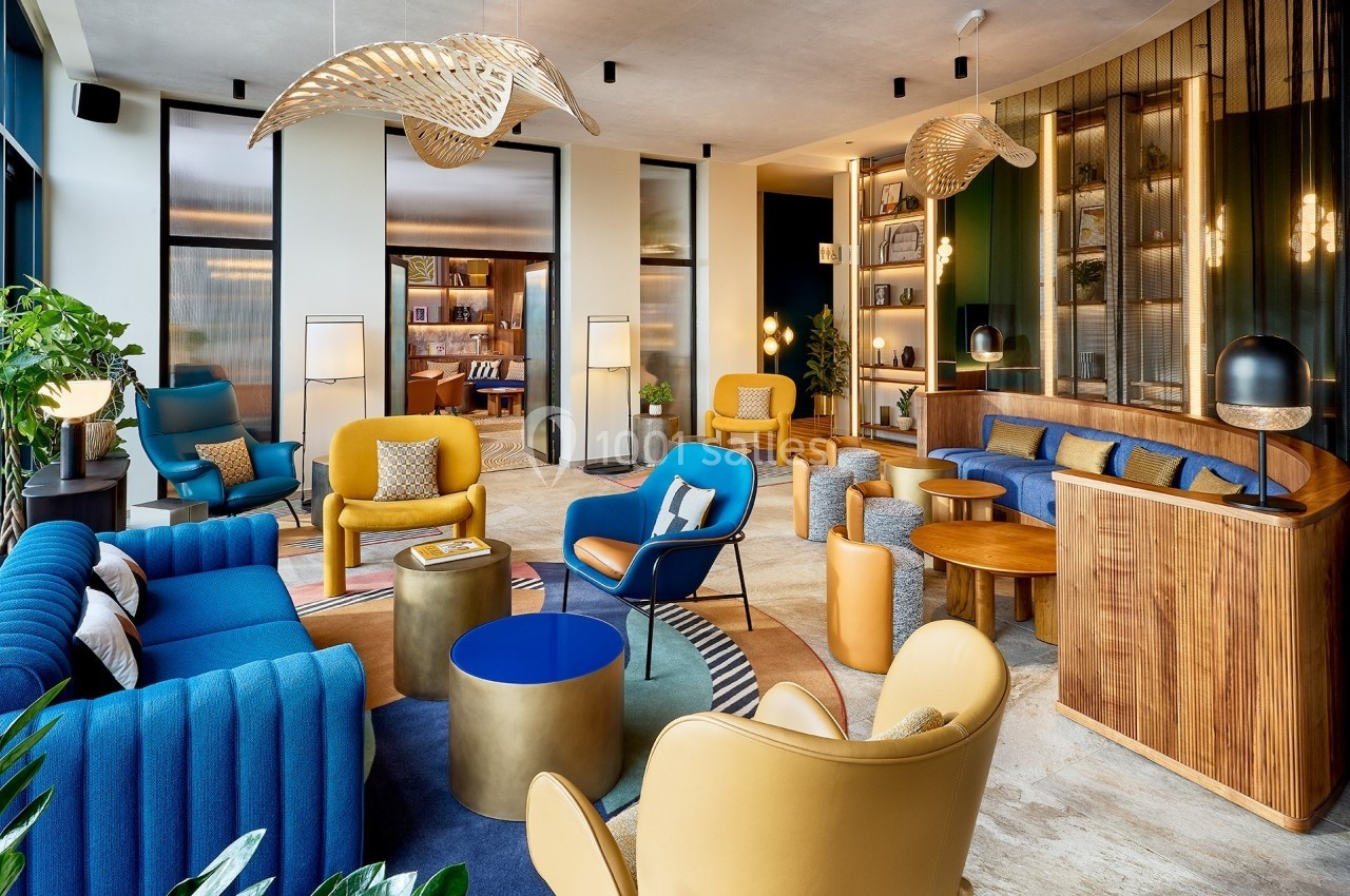 Espace lounge moderne avec fauteuils colorés, tables basses, étagères éclairées et luminaires design.