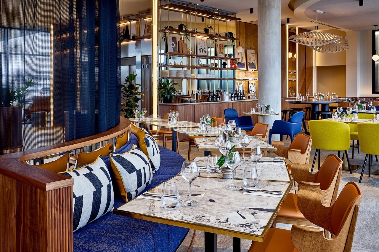 Salle de restaurant moderne avec tables en marbre, chaises colorées et décoration contemporaine.