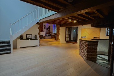 Vue d'un intérieur avec un espace ouvert, un bar en briques, un parquet clair et une mezzanine avec rambarde blanche.